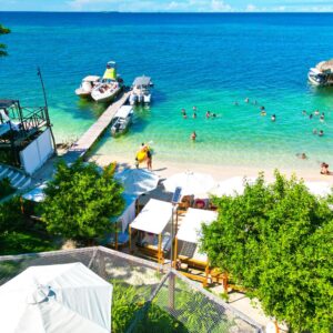 Vista de drone de la exclusiva Playa Rosario Beach con camas privadas, asoleadoras blancas y muelle flotante en el mar turquesa.